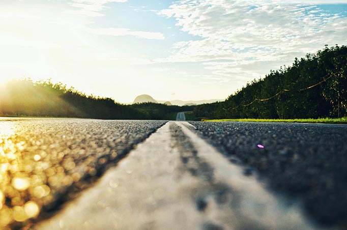 Laag standpunt van een rechte weg bij zonsopkomst, met middenstreep en groen aan weerszijden.